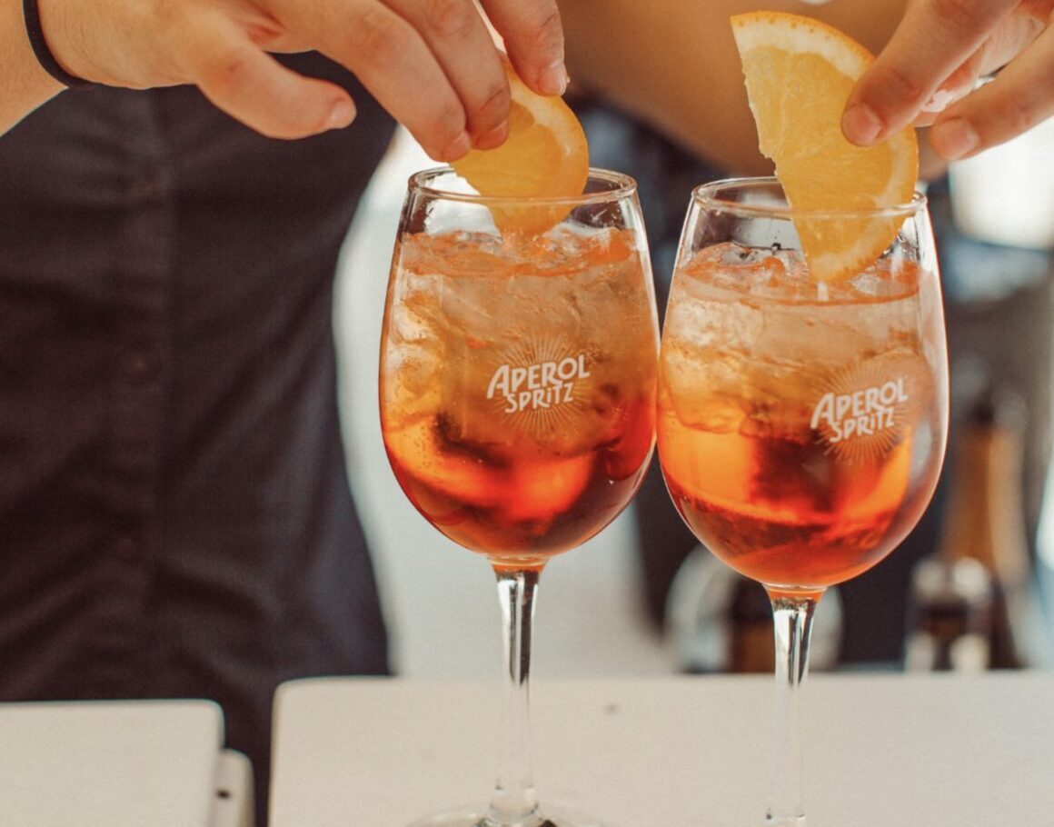 A woman places two lemon slices on two aperol spritz in glasses